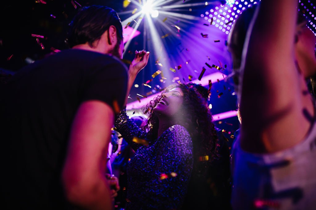 Young adult multi-ethnic group of friends dancing and enjoying a night club party with colorful confetti