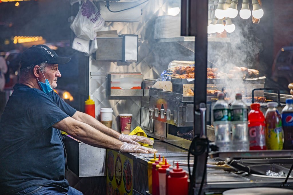 Times Square, Manhattan, New York, NY, USA - June 28, 2022: Mature man working in a steamy street kitchen at night time