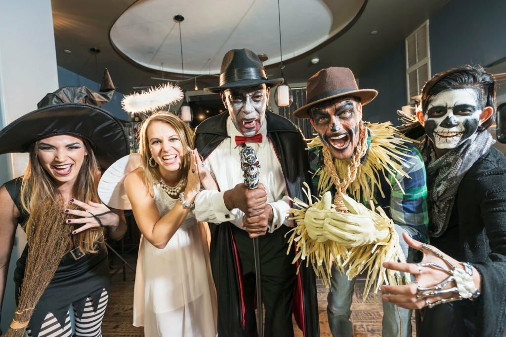 A group of five multi-ethnic men and women of mixed ages at a halloween party wearing costumes.