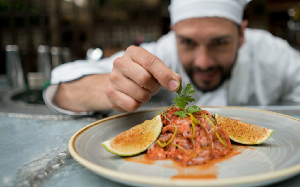 Portrait of a chef serving a plate at a restaurant and decorating it - focus on foreground
