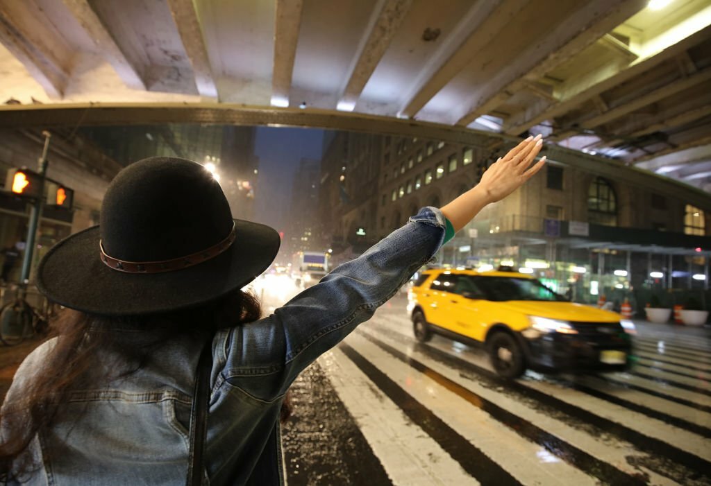 Beautiful woman hailing a taxi on Pershing Square Plaza, on 42nd Street outside Grand Central Station,  on a rainy, stormy, foggy night - Manhattan, New York City, New York, USA.