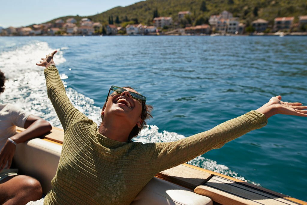 Happy young woman with arms raised in motorboat enjoying sunny day in NYC